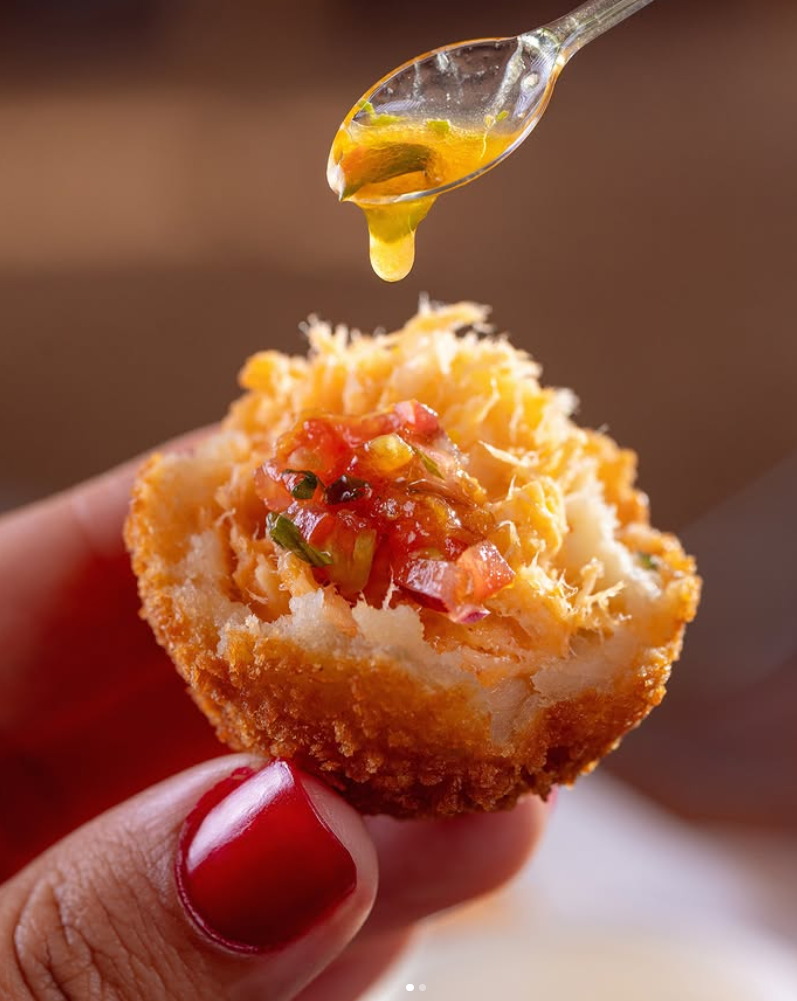 Croquetes dourados servidos com geleia da casa em tábua de madeira