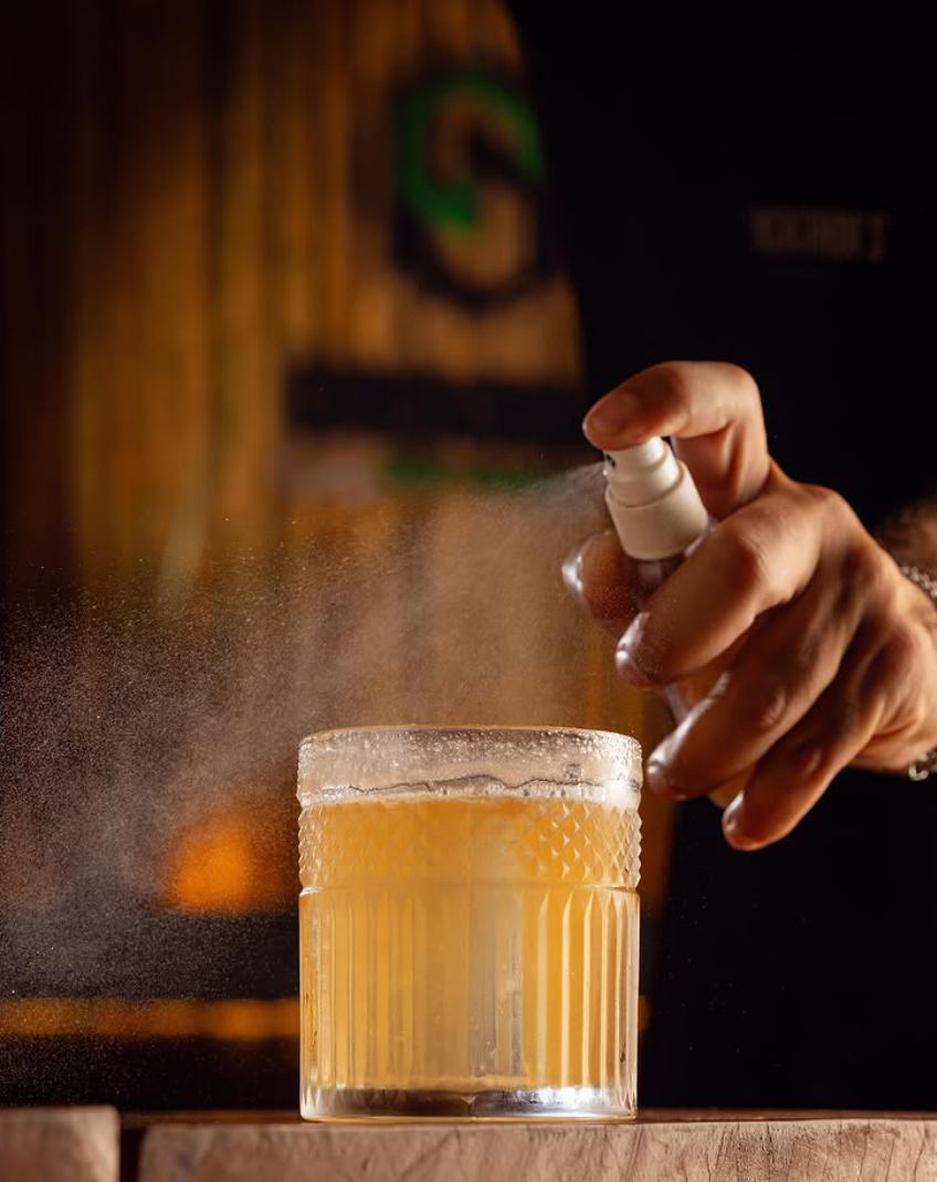 Drink autoral da casa servido em copo alto com gelo, casca de cítrico e ervas